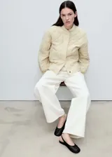 Chaqueta acolchada color crema, estilo bomber, con cuello perkins, cierre frontal con botones, dos bolsillos laterales y detalle fruncido en el bajo.