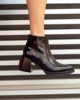 Botín corto de cuero negro, estilo cowboy moderno, con textura de cocodrilo en la caña y puntera cuadrada. Posee un tacón ancho y geométrico, y cierre lateral.