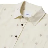 Camisa de manga corta color beige con estampado de flores pequeñas y bolsillo en el pecho. Cierre con botones marrones.