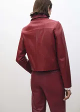 Chaqueta de cuero ovino color borgoña, de corte recto, con cuello camisero blanco, cierre frontal con botones y dos bolsillos de parche con solapa.