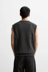 Chaleco negro de punto con cuello en V y cierre frontal con cremallera. Tiene bolsillos de ribete en la cadera y un corte relajado.