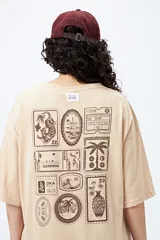 Remera color beige de corte amplio con mangas cortas y estampado de una postal con una palmera en el pecho.