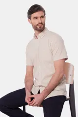 Camisa de lino color beige, de manga corta, con cuello abotonado y bolsillo en el pecho.