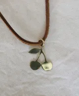 Gargantilla con dije de cerezas color bronce y tira de cuero marrón.