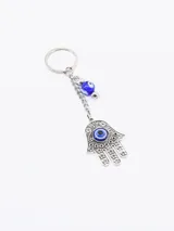 Llavero con dije de mano de Fátima (Hamsa) color plateado con ojo turco azul, y cuenta redonda azul con diseño de ojo turco.