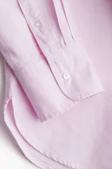 Camisa rosa de algodón Oxford con cuello clásico, botones al frente, canesú con trabilla en la espalda, corte relajado, hombros caídos, mangas largas con puños sencillos, bolsillos superiores con solapa y bajo redondeado con espalda más larga.