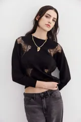 Sweater negro de tejido de punto con cuello redondo y mangas largas. Presenta recortes de encaje floral en los hombros y el frente.