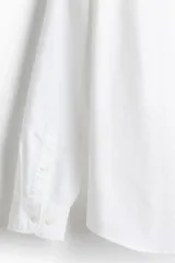 Camisa blanca de algodón Oxford con cuello americano, tapeta clásica, bolsillo superior abierto y canesú en la espalda. Mangas largas con puños abotonados y bajo levemente redondeado. Corte estándar.