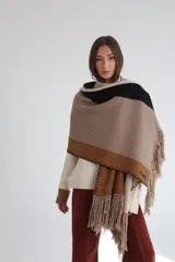Ruana tejida con diseño geométrico en bloques de color beige, azul y naranja, con flecos en el borde inferior.