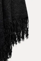 Capa tipo chal color gris oscuro confeccionada en tejido de punto con lana y alpaca. Tiene cuello alto y terminación con flecos.