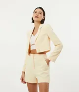 Blazer cropped color amarillo pastel, de crepé con forro de poliéster, cuello solapa, manga larga y cierre frontal con botón en forma de corazón.