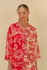 Camisa con estampado floral en tonos rojo y blanco, confeccionada en tejido ligero. Presenta cuello clásico, mangas largas y cierre frontal con botones.