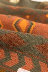 Buzo tejido con cuello redondo, mangas largas y diseño con motivos geométricos en tonos marrón, naranja y verde.