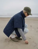 Poncho acolchado color mostaza con cuello alto y abertura frontal con cierre. Presenta un patrón capitoné de formas ovaladas y bolsillos delanteros.