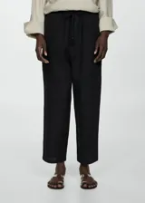 Pantalón negro de lino con diseño crop y jogger, tiro medio, cintura elástica con lazo, dos bolsillos laterales y dos bolsillos de ribete en la parte posterior.