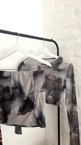Conjunto de top corto de mangas largas y falda corta, ambos de tela traslúcida con estampado de nubes en tonos grises.