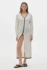 Túnica tipo vestido tejido calado color blanco, con cuello en V y ribete negro, abotonada adelante, de largo midi y con cortes a los lados.