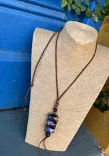 Colgante con cordón de cuero marrón ajustable, cuentas de madera y cuentas de cerámica con diseño abstracto en tonos marrones y azules.