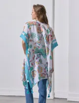 Kimono tejido con estampado floral multicolor, terminación de ruedo con borlas y mangas cortas con borde celeste.
