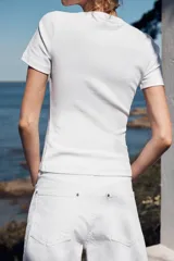 Camiseta blanca de corte slim fit, escote redondo y manga corta. Presenta apliques de fornitura a contraste en el delantero.