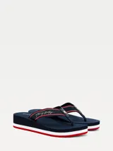 Ojotas de mujer marca Tommy Hilfiger con suela de cuña. Cuentan con tiras de nailon trenzado en color azul marino con detalles en rojo y blanco, firma de la marca bordada y logo metálico. La suela de goma presenta franjas decorativas en los colores distintivos de la marca.
