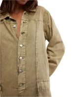 Mono largo color verde oliva, de denim liviano con efecto desgastado. Tiene corte holgado, largo hasta los tobillos, mangas largas, cuello camisero y cierre frontal con botones metálicos. Incluye bolsillos amplios y costuras visibles.