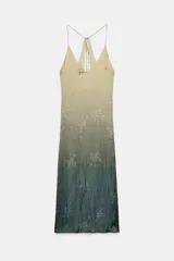 Vestido midi lencero con escote pico y tirantes finos ajustables con lazada en la espalda. Presenta un efecto degradado de color, pasando de un tono beige/amarillento claro en la parte superior a un verde azulado oscuro en el bajo. El tejido tiene un estampado sutil de rosas en relieve.