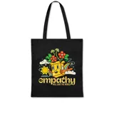 Bolso de tela negro, tipo tote bag, con estampado frontal de estilo retro. El diseño muestra una caja sonriente de la que brotan flores, junto al sol y nubes, con el texto "empathy WILL SAVE THE WORLD".