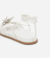 Sandalias planas blancas de cuero sintético, con tiras finas, puntera redonda, lazo para atar al tobillo y maxi flor aplicada en la capellada.