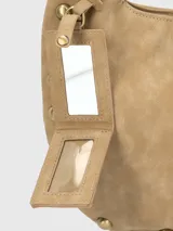 Cartera tipo hobo color beige de gamuza sintética con tachas doradas en el borde. Tiene un asa de hombro y un dije colgante con el logo de la marca.