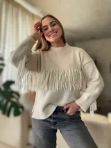Sweater de lana color crema, con cuello redondo y mangas largas. Presenta una banda horizontal de flecos en el pecho.