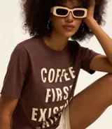Remera marrón de algodón con cuello redondo y mangas cortas. Estampa frontal con la frase "Coffee First Existin Later" en letras blancas.