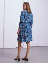 Vestido corto de rayón con estampado floral en tonos azules y blancos. Tiene escote en V, mangas 3/4 con puño, cintura con lazo de ajuste y borlas.