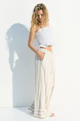 Pantalón de lino color crudo con rayas verticales color beige. Corte holgado, cintura elástica con cordón ajustable y piernas anchas extralargas.