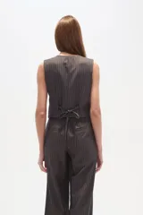 Chaleco de vestir sin mangas, color negro con finas rayas verticales blancas. Presenta escote en V, cierre frontal con botones y bolsillos falsos a la altura de la cintura.