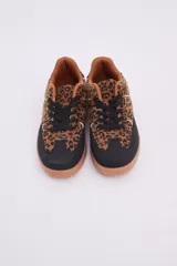 Zapatillas bajas de cuero sintético con estampado animal print, puntera y cordones negros, suela color caramelo y detalle en el talón color blanco.
