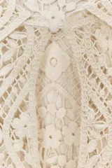Vestido corto color crudo confeccionado en tejido tipo crochet con diseño geométrico floral. Tiene cuello solapa, abertura con botón en la parte superior y mangas largas acampanadas.