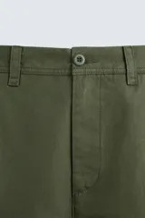 Pantalón chino color verde militar, de corte recto, con bolsillos laterales y traseros de vivo. Cierre frontal con cremallera y botón.