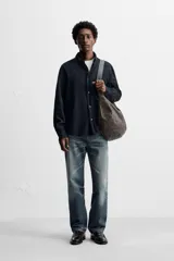 Camisa azul de algodón con textura chambray, corte regular fit, cuello abotonado, manga larga con puños abotonados, bolsillo de parche en el pecho y cierre frontal con botones.