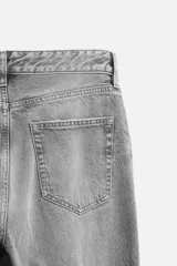 Pantalón de jean negro con efecto lavado, corte flare, cinco bolsillos, cierre frontal con cremallera y botón, y bajo con acabado irregular.