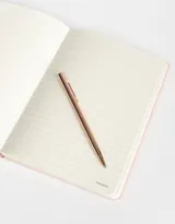 Set de librería que incluye un cuaderno A5 forrado en PU rosa pastel con elástico y una lapicera metálica de tinta negra.