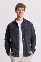Camisa de jean de manga larga, color gris oscuro lavado, con cuello y botones a presión blancos. Presenta dos bolsillos frontales con solapa y pespuntes visibles.