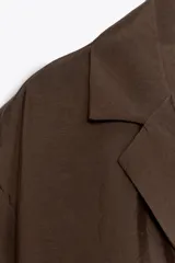 Camisa marrón de cuello solapa y escote pico con manga corta. Bolsillos de plastrón en pecho. Cierre frontal con botones.