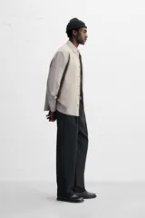 Camisa color crema de corte relaxed fit, confeccionada en tejido de mezcla de algodón suave al tacto. Tiene cuello solapa, manga larga con puños abotonados, un bolsillo de parche en el pecho y cierre frontal con botones.