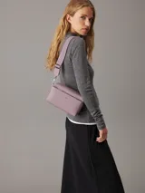Bandolera Calvin Klein modelo Must, color lila, con correa ajustable y logo plateado en el frente. Incluye bolsillo exterior con cierre y bolsillo interior.
