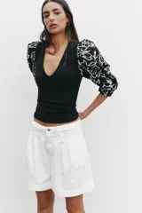 Top negro de escote pico con detalle de fornitura y mangas 3/4 abullonadas con estampado de flores bordadas.