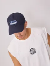 Gorra de lona lavada color beige con visera verde y parche con el logo de Rusty en el frente.