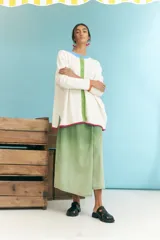 Cardigan blanco de algodón con cuello redondo, cierre frontal con botones verdes, puños con ribete naranja y ruedo con ribete fucsia.