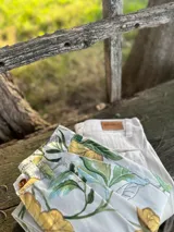 Pantalón corto de vestir color crudo con estampado de hojas verdes y amarillas.