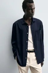 Pantalón chino negro de corte relajado (relaxed fit) con tiro medio, confeccionado en algodón con elasticidad. Presenta bolsillos delanteros y bolsillos traseros de vivo, con cierre frontal de cremallera y botón.